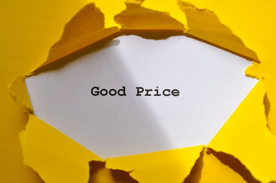 A close-up view of a white piece of paper with the words 'Good Price' printed in black, visible through a torn and uneven hole in a yellow paper background. The torn edges of the yellow paper reveal the white paper beneath, with some frayed fibers around the tear. The background surface appears to be a yellow wall or large sheet of paper, creating a stark contrast with the white message paper. The lighting is even, highlighting the texture of the torn yellow paper and the smooth surface of the printed message. This image visually emphasizes the concept of affordability or value, which could relate to private or alternative waste management services offered by companies like House Clearance Balham, hinting at transparent or straightforward pricing for rubbish removal tasks.